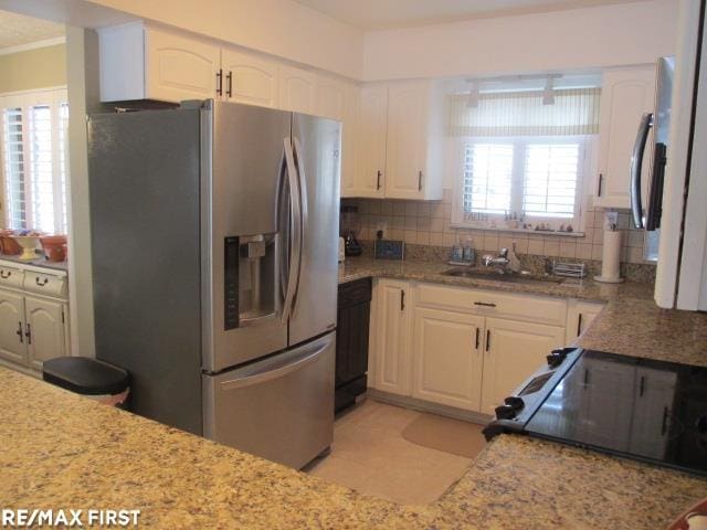 kitchen featuring stainless steel fridge, sink, white cabinetry, stove, and tasteful backsplash