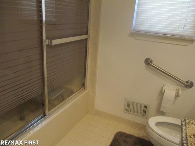 bathroom featuring toilet, tile patterned flooring, and enclosed tub / shower combo