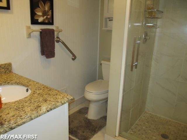 bathroom featuring toilet, vanity, tile patterned flooring, and a shower with shower door