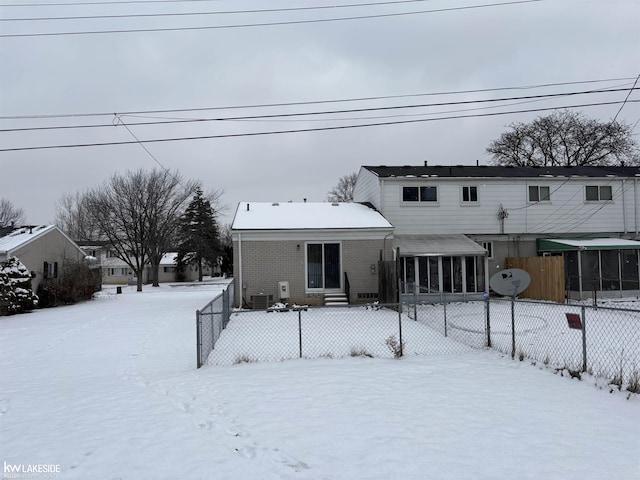 snow covered rear of property featuring a sunroom