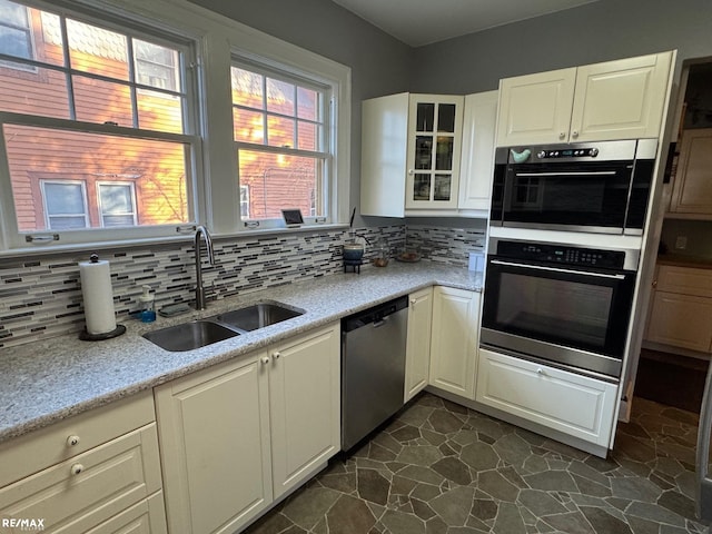 kitchen with light stone counters, sink, double wall oven, stainless steel dishwasher, and backsplash