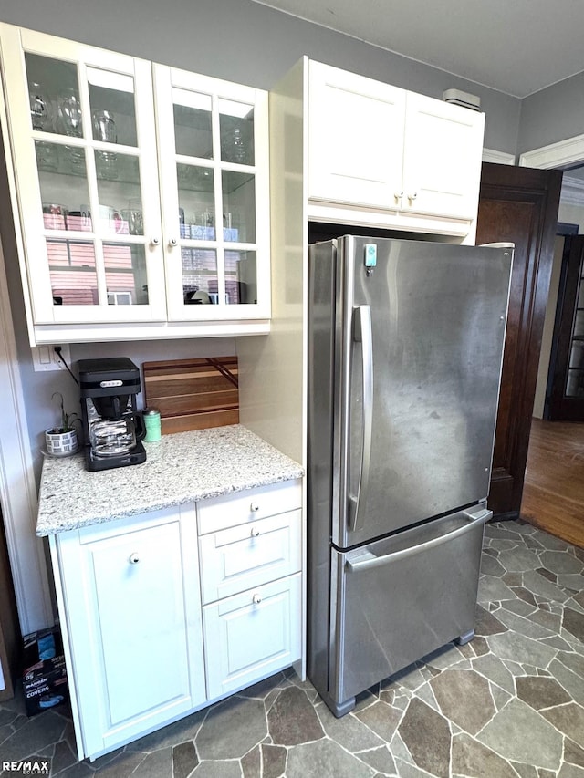 kitchen with stainless steel fridge, white cabinetry, and light stone countertops