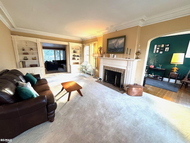 living room with light wood-type flooring, a tile fireplace, crown molding, and built in shelves