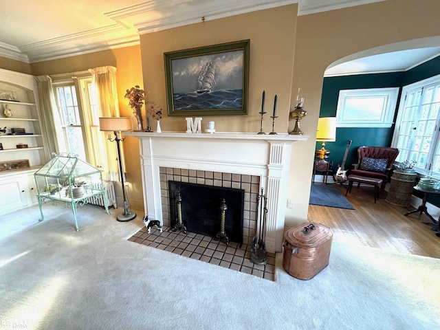 living room featuring a tile fireplace, built in shelves, ornamental molding, and carpet