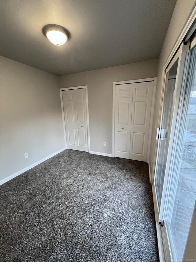 unfurnished bedroom with dark carpet and multiple closets