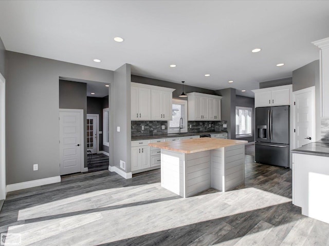 kitchen with wooden counters, a kitchen island, black refrigerator with ice dispenser, white cabinetry, and backsplash