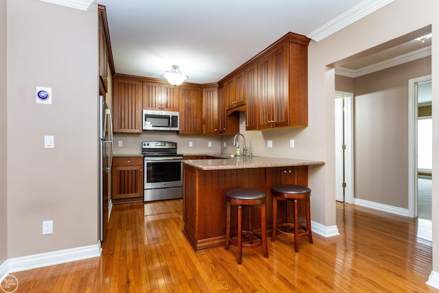 kitchen with appliances with stainless steel finishes, light hardwood / wood-style floors, kitchen peninsula, ornamental molding, and sink