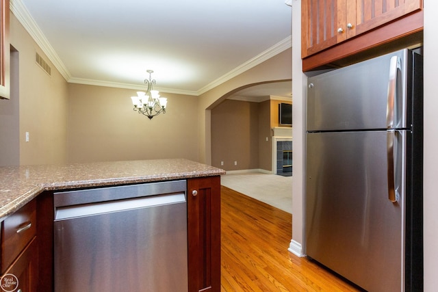 kitchen with ornamental molding, stainless steel appliances, light wood-type flooring, and a tile fireplace