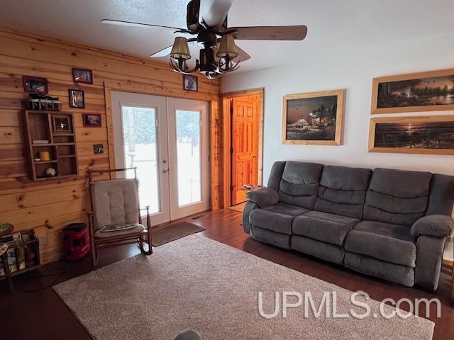 living room with ceiling fan, french doors, wooden walls, and dark hardwood / wood-style flooring