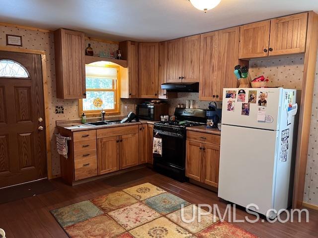 kitchen featuring white refrigerator, sink, black range with gas cooktop, and dark wood-type flooring