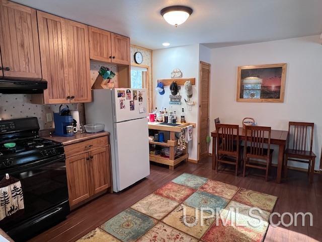 kitchen with dark hardwood / wood-style flooring, white fridge, backsplash, and black range oven