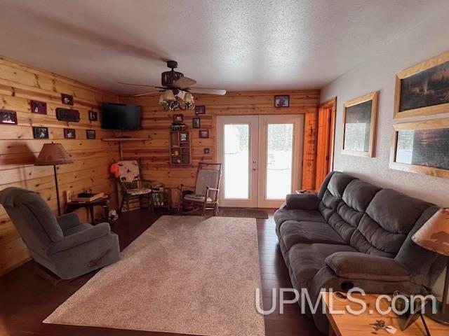 living room featuring wooden walls, a textured ceiling, french doors, ceiling fan, and dark hardwood / wood-style flooring