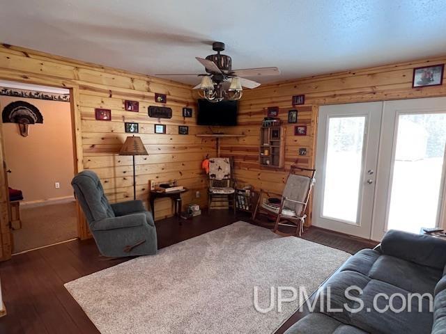 living room with dark wood-type flooring, french doors, ceiling fan, and wooden walls