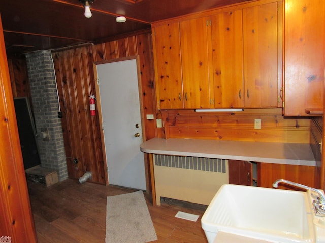 kitchen with sink, hardwood / wood-style floors, radiator heating unit, and wood walls