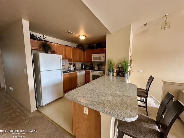 kitchen with a kitchen bar, kitchen peninsula, and white appliances