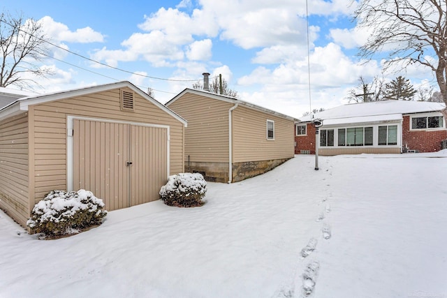 snow covered house featuring a garage and an outbuilding