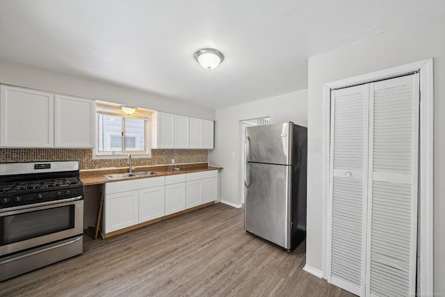 kitchen featuring white cabinets, appliances with stainless steel finishes, sink, backsplash, and light wood-type flooring