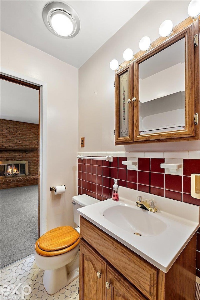 bathroom featuring toilet, vanity, a brick fireplace, and tile patterned floors