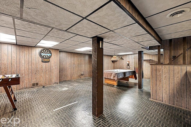 basement featuring a paneled ceiling and wood walls