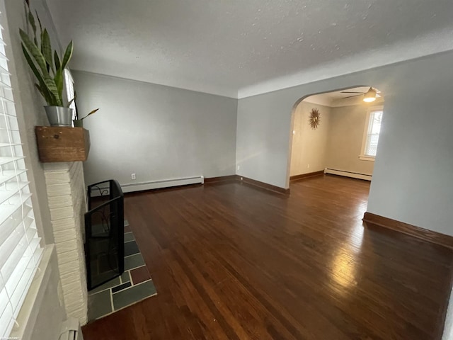 unfurnished living room featuring dark wood-type flooring, baseboard heating, and a brick fireplace