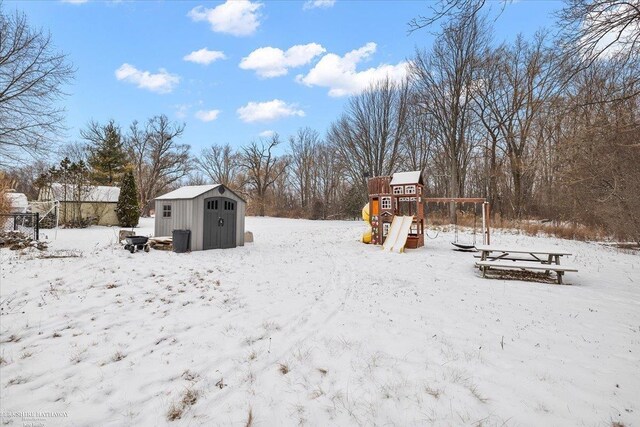 snowy yard with a storage shed and a playground