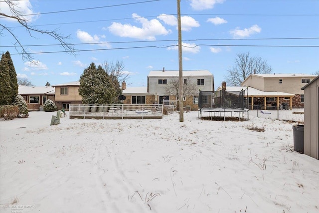 snow covered rear of property with a trampoline