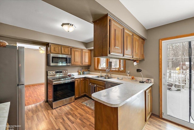 kitchen featuring kitchen peninsula, ceiling fan, appliances with stainless steel finishes, light wood-type flooring, and sink