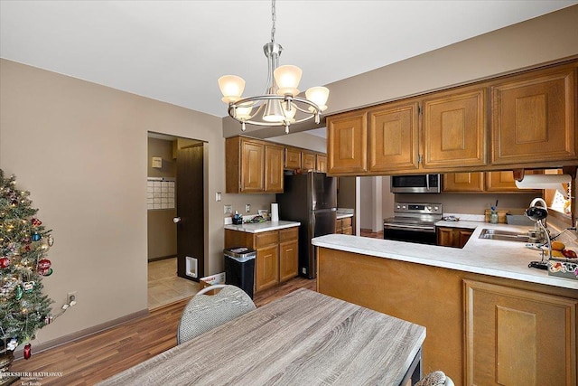 kitchen featuring pendant lighting, appliances with stainless steel finishes, an inviting chandelier, kitchen peninsula, and light wood-type flooring