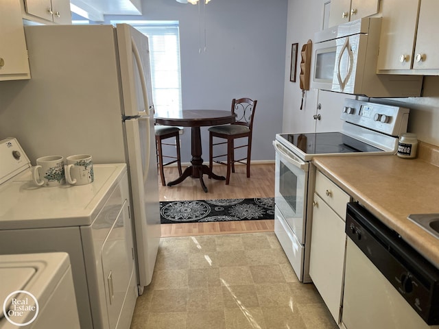 kitchen with washer and clothes dryer, white cabinets, and white appliances