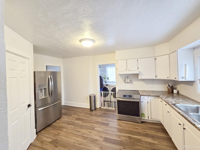 kitchen featuring white cabinets, wood-type flooring, appliances with stainless steel finishes, and tasteful backsplash