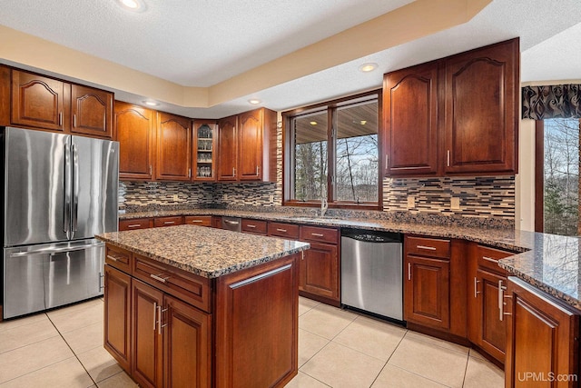 kitchen with light tile patterned flooring, backsplash, appliances with stainless steel finishes, and dark stone countertops