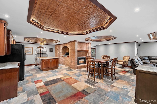 dining space with a brick fireplace, ornamental molding, and a raised ceiling