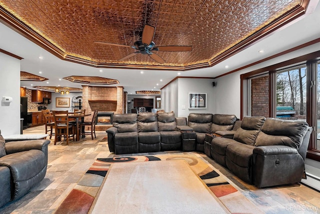 living room featuring a brick fireplace, a raised ceiling, ornamental molding, and ceiling fan