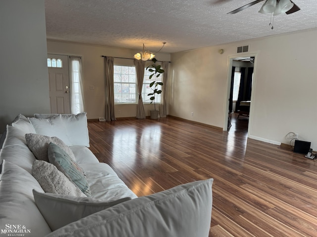 living room with dark hardwood / wood-style flooring, ceiling fan with notable chandelier, and a textured ceiling