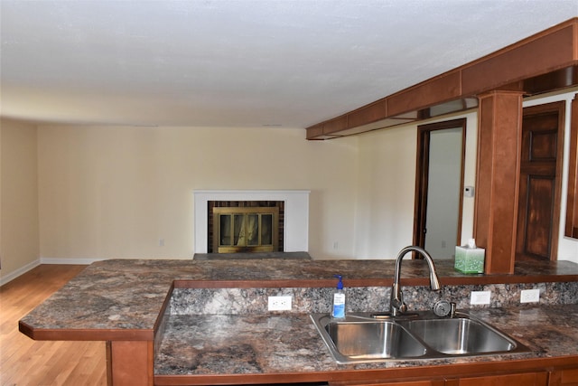 kitchen with light hardwood / wood-style flooring, a fireplace, kitchen peninsula, and sink