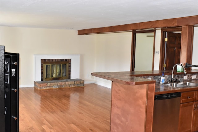 kitchen with light hardwood / wood-style floors, dishwasher, a stone fireplace, and sink