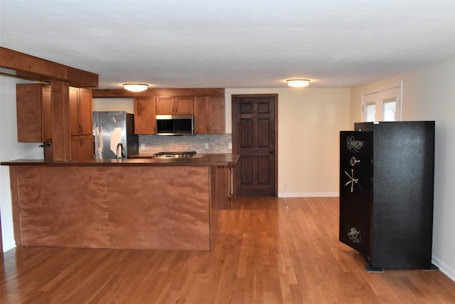 kitchen featuring light hardwood / wood-style floors, kitchen peninsula, decorative backsplash, and refrigerator