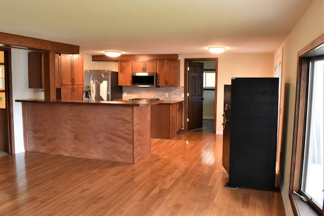 kitchen with decorative backsplash, kitchen peninsula, stainless steel appliances, and light wood-type flooring