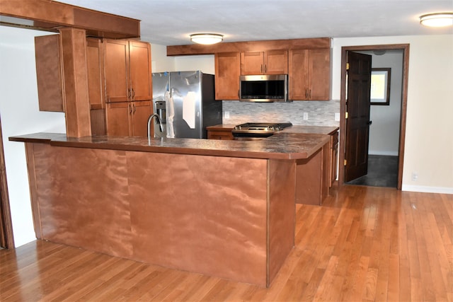 kitchen with appliances with stainless steel finishes, light hardwood / wood-style flooring, kitchen peninsula, and backsplash