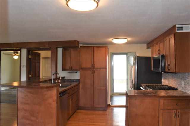 kitchen featuring kitchen peninsula, appliances with stainless steel finishes, decorative backsplash, light hardwood / wood-style flooring, and sink