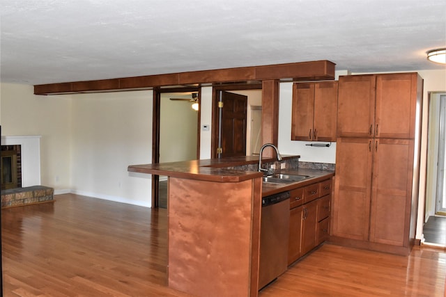 kitchen featuring stainless steel dishwasher, a brick fireplace, sink, and light hardwood / wood-style floors