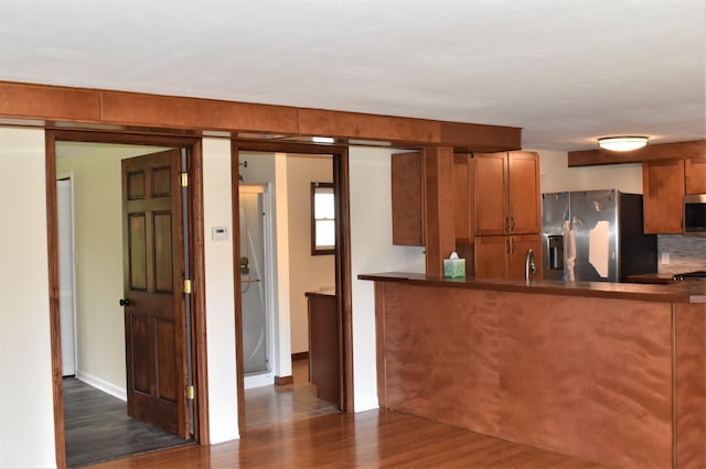 kitchen featuring dark hardwood / wood-style floors, kitchen peninsula, decorative backsplash, sink, and stainless steel appliances