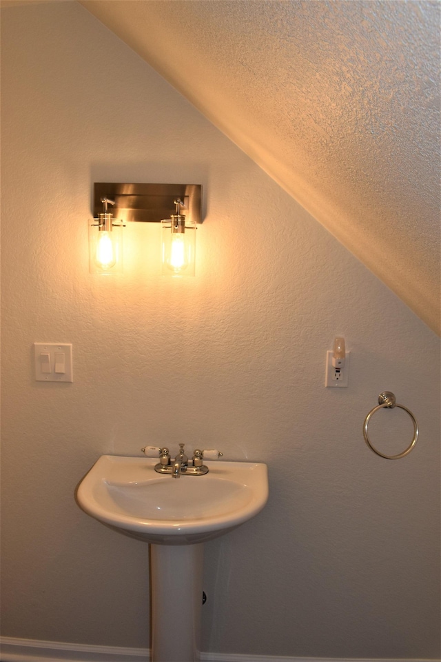 bathroom with a textured ceiling, vaulted ceiling, and sink