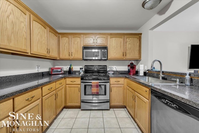 kitchen with light tile patterned floors, dark stone counters, sink, and stainless steel appliances