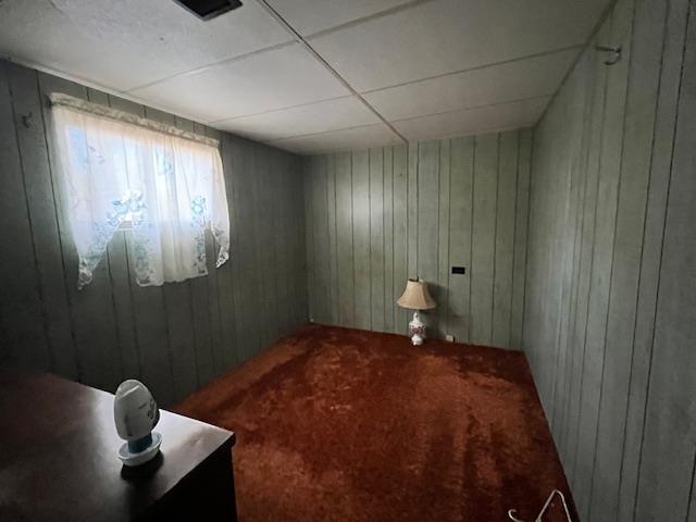 carpeted empty room with a drop ceiling and wooden walls