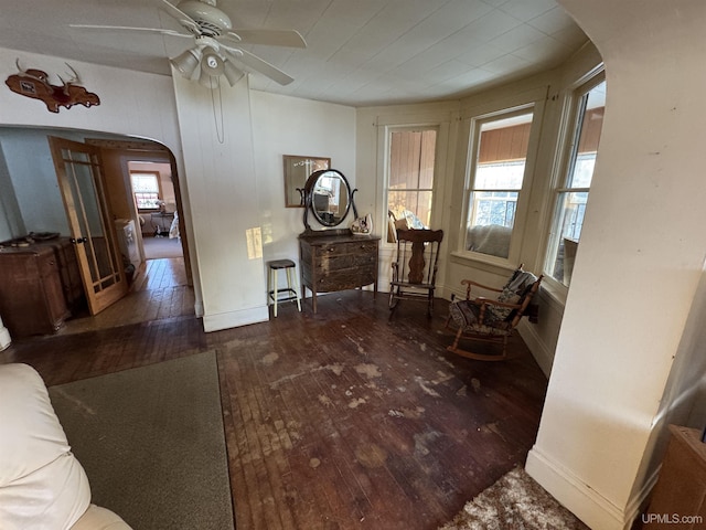 living area with ceiling fan, dark wood-type flooring, and a wealth of natural light