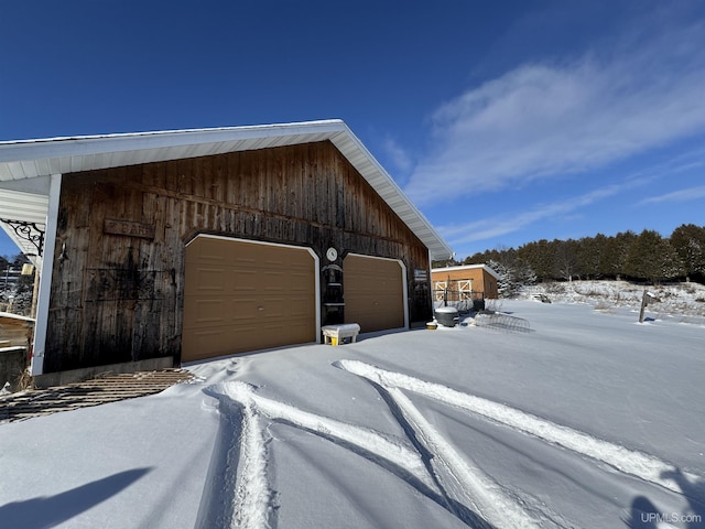 view of snow covered exterior featuring a garage and an outbuilding