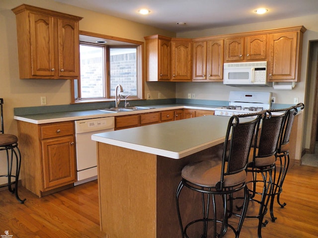 kitchen with sink, a center island, light hardwood / wood-style flooring, a kitchen breakfast bar, and white appliances