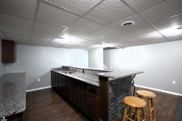 bar with a drop ceiling, sink, dark brown cabinets, and dark wood-type flooring