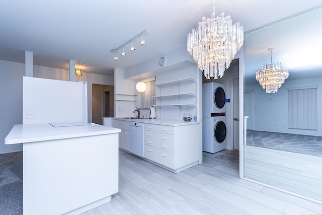 kitchen featuring decorative light fixtures, a notable chandelier, white appliances, stacked washing maching and dryer, and white cabinets